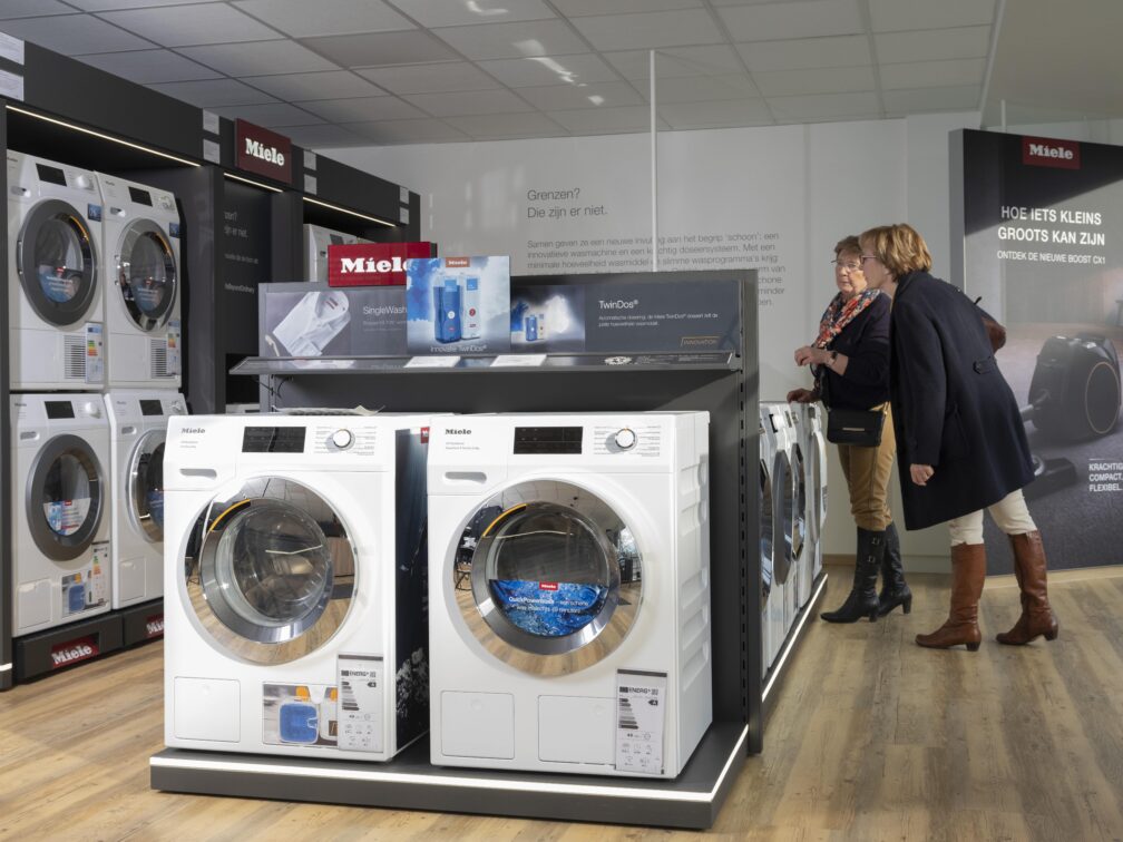 Twee tevreden klanten bekijken het gamma aan wasmachines, droogkasten en strijkstations in de toonzaal van Miele Center Bingé